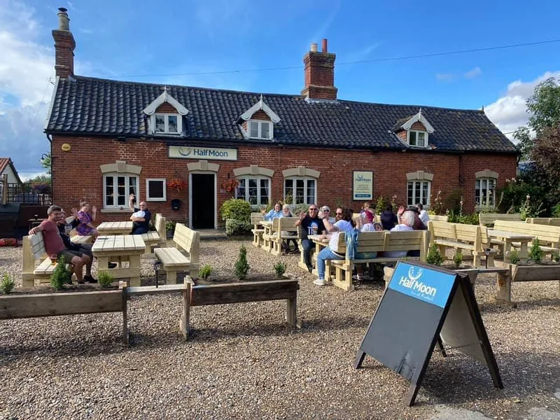 The Half Moon from The Street: a red-brick pub with picnic benches out front and its sign by the road